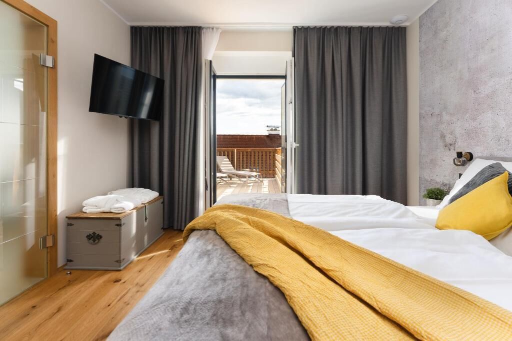 A hotel room with a bed, a TV, a small cabinet, and a balcony view.