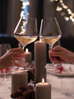 Two people holding wine glasses with a candle and pine cones on a table.