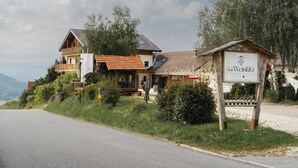 A two-story building with a balcony, a signboard, and a view of the mountains. - Das Weinkitz  (Kitzeck im Sausal)