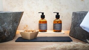 A bathroom vanity with two bottles of Vinoble Cosmetics hair and body shampoo and liquid soap, a wooden bowl, and a black mat. - Das Weinkitz  (Kitzeck im Sausal)