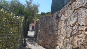 A narrow stone pathway flanked by a wire fence and a stone wall, leading to a building with a sloped roof. - Ftam-corn01 in Tamarispa (Budoni)