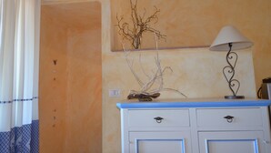 A room with a blue and white dresser, a lamp, and a wall-mounted vase with branches. - Ftam-corn01 in Tamarispa (Budoni)