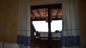 A room with a bed, a table, and chairs, and a view through a glass door to an outdoor area with a table and chairs. - Ftam-corn01 in Tamarispa (Budoni)