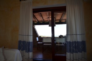A room with a bed, a table, and chairs, and a view through a glass door to an outdoor area with a table and chairs. - Ftam-corn01 in Tamarispa (Budoni)