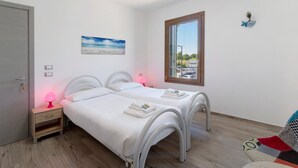 Een slaapkamer met twee bedden, een nachtkastje met lamp, een raam met uitzicht en een schilderij aan de wand.