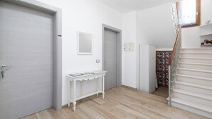 Een hal met een houten vloer, een witte deur, een klein tafeltje met tijdschriften en een trap met een stenen muur.