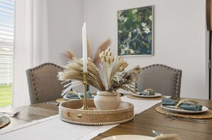 A dining table with a candle centerpiece, a vase with dried flowers, and a painting on the wall. - Luxe 3BR | Long & Short Stays l Walk to Eastport | Golf Cart (Sumterville)