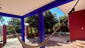 A covered patio area with a hammock, a wooden bench, and a red wall.