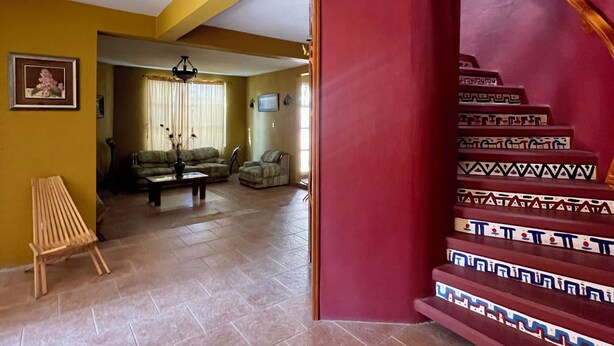 A living room with a sofa, a coffee table, and a bench. There is a staircase with patterned steps.