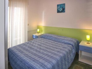 Quarto com cama, duas mesas de cabeceira, um criado-mudo, janela com cortinas e um quadro na parede.