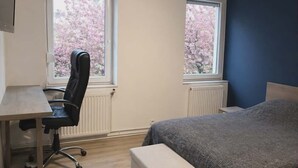 Quarto com cama, escrivaninha e duas janelas.