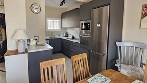 A modern kitchen with a refrigerator, microwave, and oven. There is a dining table with chairs and a decorative plate. - Detached, newly refurbished, 3 bed house with parking, 2 min walk from the beach (Fuengirola)