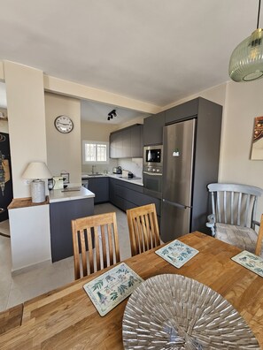 A modern kitchen with a refrigerator, microwave, and oven. There is a dining table with chairs and a decorative plate. - Detached, newly refurbished, 3 bed house with parking, 2 min walk from the beach (Fuengirola)