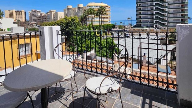 A balcony with a table and chairs, overlooking a cityscape with buildings and palm trees. - Detached, newly refurbished, 3 bed house with parking, 2 min walk from the beach (Fuengirola)