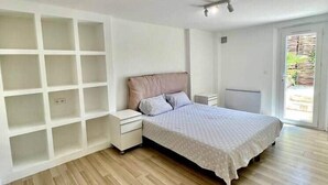 Ein Schlafzimmer mit Bett, Nachttisch, integriertem Bücherregal und einer Glastür zum Außenbereich.