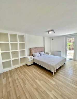 Une chambre comprenant un lit, une table de chevet, une bibliothèque intégrée et une porte-fenêtre coulissante donnant sur un espace extérieur.