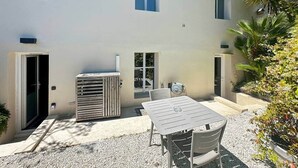 Ein Gebäude mit einer Terrasse, einem Tisch, Stühlen, einer Klimaanlage und einem kleinen Garten.