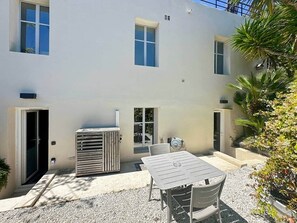Un bâtiment doté d’un patio, d’une table, de chaises, d’un climatiseur et d’un petit jardin.