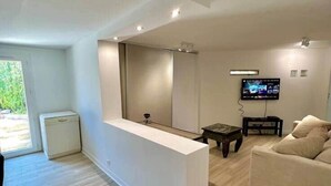 Ein modernes Wohnzimmer mit einem weißen Empfangstresen, einem wandmontierten Flachbildfernseher, einem beigen Sofa und einem Holzboden.