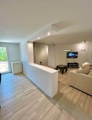 Un salon moderne avec un comptoir d’accueil blanc, un téléviseur à écran plat fixé au mur, un canapé beige et un plancher en bois.