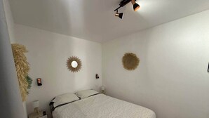 Quarto com cama, mesa de cabeceira, decoração na parede e luminária no teto.