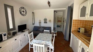 Uma cozinha compacta com mesa de jantar, armários brancos, micro-ondas e um relógio na parede.