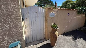 Uma entrada protegida com cerca branca de piquete, um vaso de planta e uma placa na parede.
