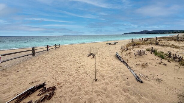 Een strand met een houten hek, een bankje en een heldere lucht.