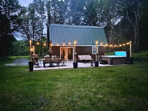 A wooden cabin with a metal roof, outdoor seating, and string lights. - Private Cottage with Hot Tub Near Elk Mountain (Thompson Township)