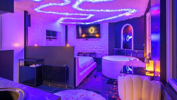 A modern room with a bed, a bathtub, a TV, and a neon sign. - L'Etage des nuages - Jacuzzi & precious moments (La Flèche)