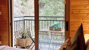 Habitació de fusta amb una porta corredissa de vidre que dona a un balcó exterior amb una taula, cadires i una planta en test.