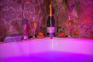 Une bouteille de champagne, deux verres et un macaron posés sur un mur de pierre.