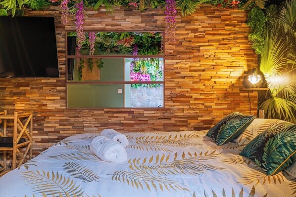 A bedroom with a bed, a TV mounted on the wall, and a window with a view of greenery.