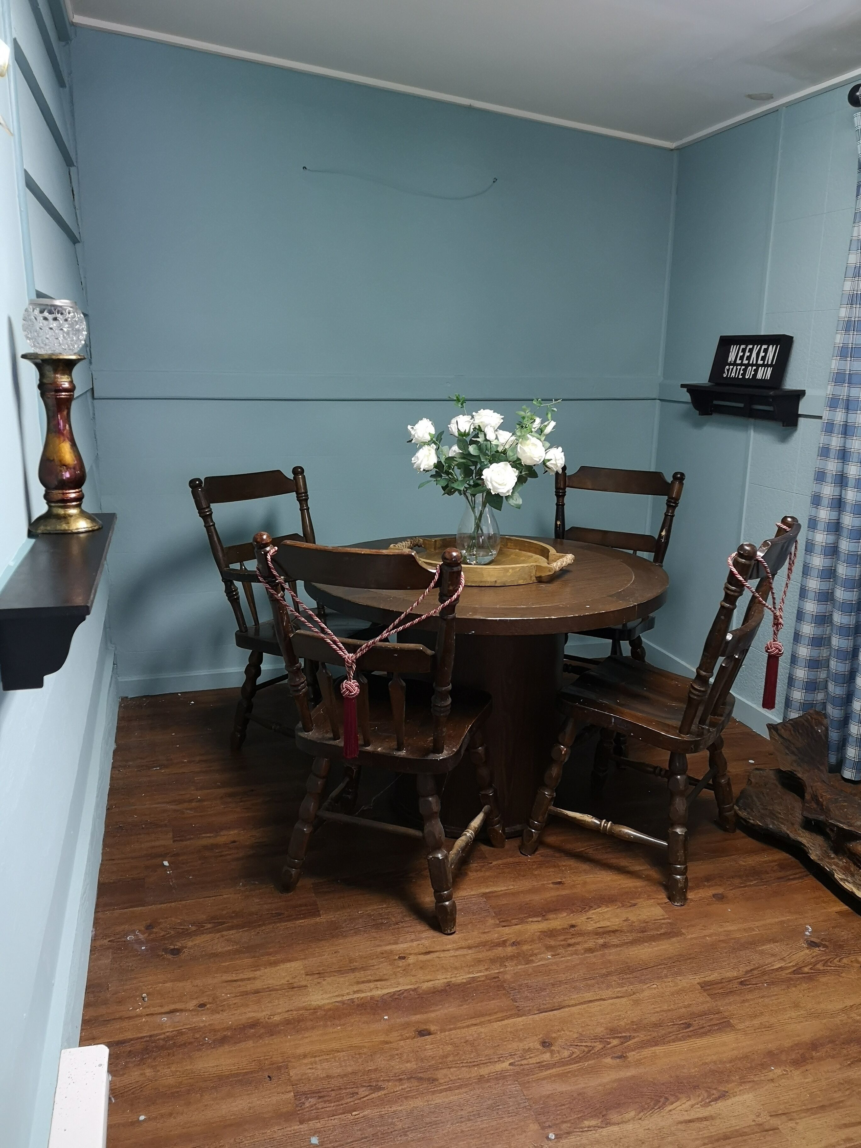 A dining area with a round wooden table, four chairs, a vase with white flowers, and a decorative candle holder.