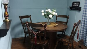 Un comedor con una mesa redonda de madera, cuatro sillas, un florero con flores blancas y un candelabro decorativo.