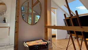 Een kamer met een houten plafond, een ronde spiegel, een bed en een schilderij op een lessenaar.