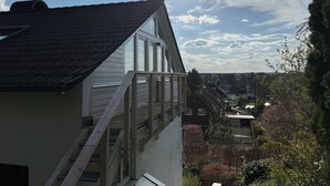 Een woongebouw met een schuin dak, een zichtbare trap en uitzicht op omliggende huizen en bomen.