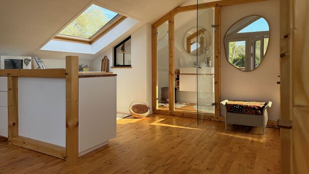 Een modern interieur met dakraam, houten balken, een glazen scheiding en een ronde spiegel.