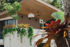 A modern building with a sloped roof, a ceiling fan, and a planter with various plants. - Intimate casita with king bed, modern bath, kitchenette, mountain views, and outdoor patio. (Manuel Antonio)