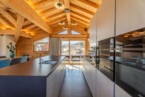 A modern kitchen with wooden beams, a large island, and a view of a mountain village. - 2nd floor, hammam, balcony, fireplace or stove, parking, 190m², Les Gets (Les Gets)