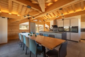 A wooden interior with a dining table and chairs, a kitchen with modern appliances, and large windows. - 2nd floor, hammam, balcony, fireplace or stove, parking, 190m², Les Gets (Les Gets)