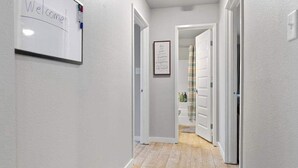 A hallway with a whiteboard displaying 'Welcome,' a framed quote on the wall, and a wooden floor. - Cozy Stay_2Bedrooms_Work Space_Near Attractions (Fort Smith)