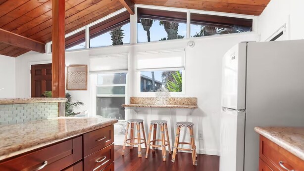 Une cuisine avec des meubles en bois, un réfrigérateur blanc et une fenêtre donnant sur un paysage tropical.