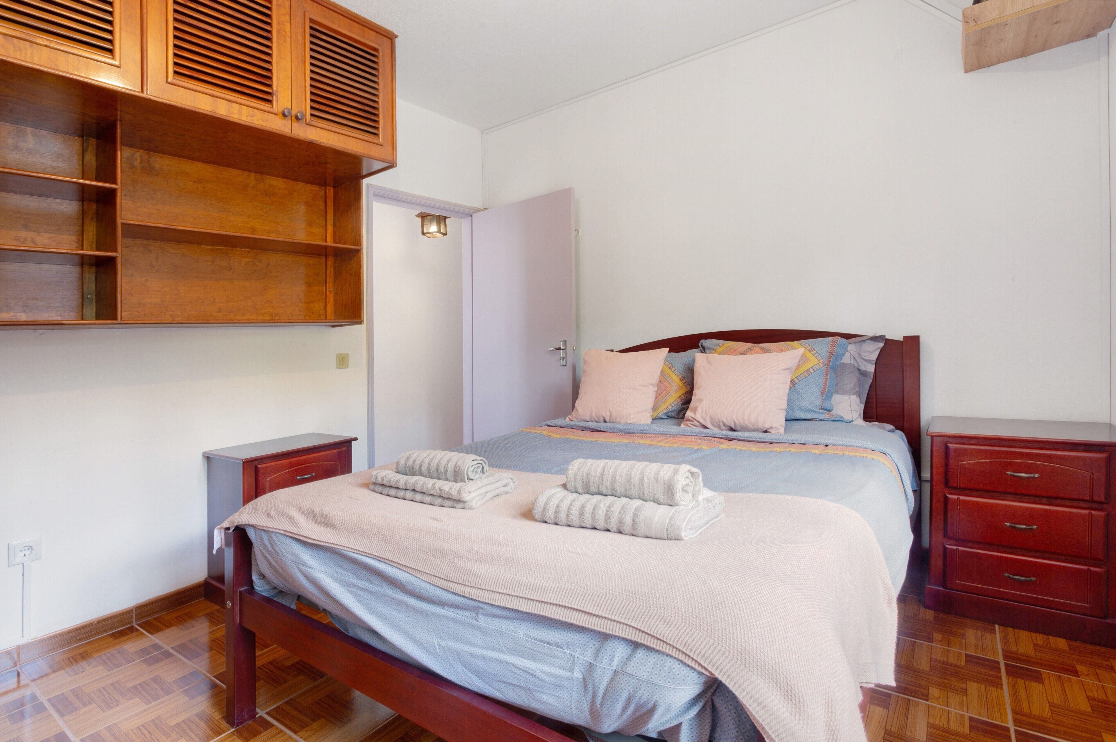 A bedroom with a bed, wooden cabinets, a nightstand, and a wardrobe.
