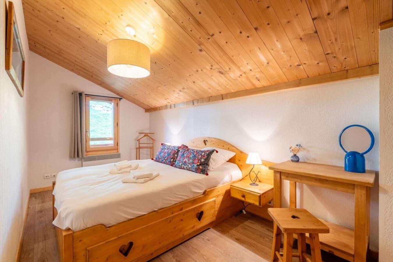 A wooden bed with a headboard, a bedside table, a lamp, and a small stool.