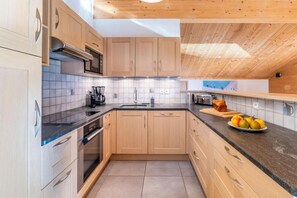 A modern kitchen with wooden cabinets, a black countertop, and a tiled backsplash. - 4th floor, balcony, parking, ski locker, 132m², Le Grand Bornand (Le Grand-Bornand)