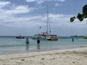 Ein Strand mit Booten, einer Segelyacht und Menschen im Wasser.