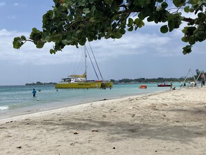 Ein Strand mit einem gelben Boot namens 'JANWEST SEA CAT LII', das in der Nähe des Ufers vor Anker liegt.