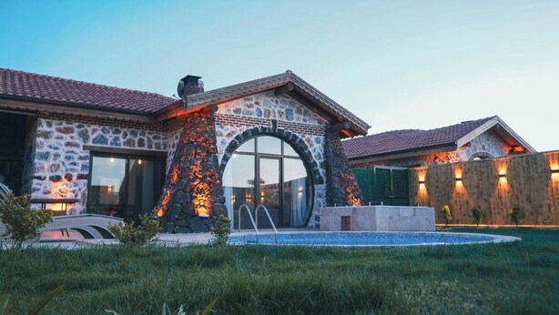 Une maison en pierre dotée d’une piscine, d’un patio couvert et d’une grande entrée en arc de cercle.