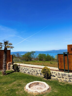 A backyard with a stone wall, a wooden fence, a palm tree, and a view of the sea. - Liva Villa (İznik)